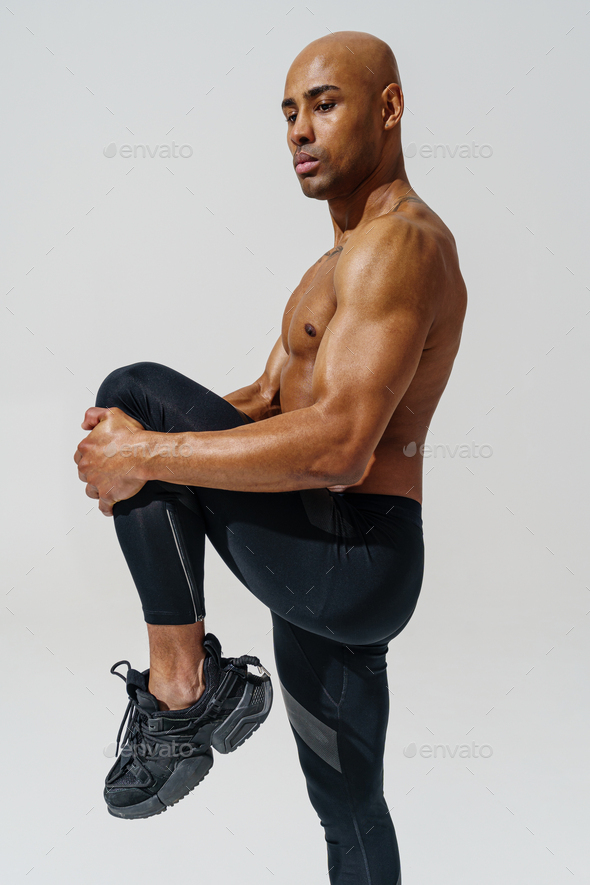 Athletic man with naked torso doing leg stretching exercises before workout  on studio background Stock Photo by KostiantynVoitenko