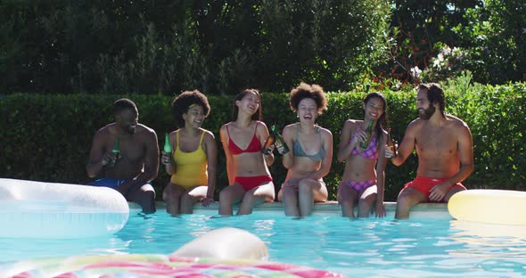 Diverse group of friends sitting at the poolside drinking beer and talking alt