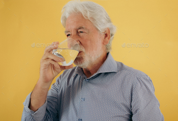 Handsome white-haired senior man drinking a glass of water - caucasian bearded elderly man