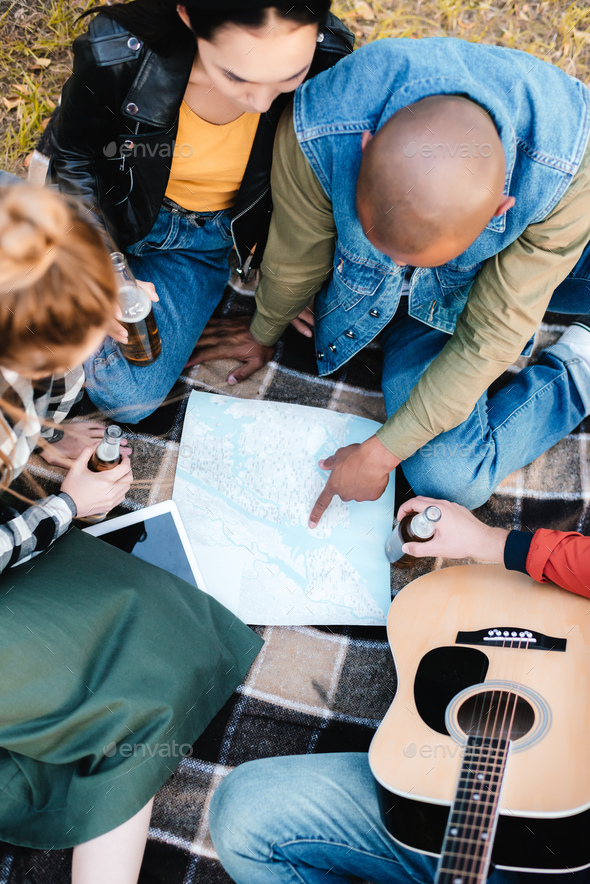 overhead view of multicultural friends pointing at map while sitting on
