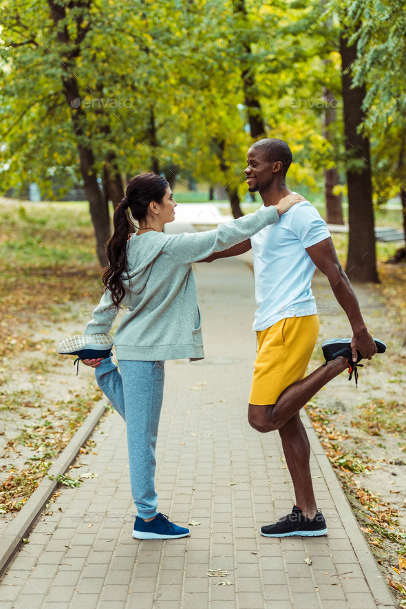 Multicultural couple stretching on a road at the park Stock Photo by ...