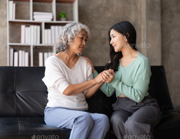 Daughter talking to sad mother holding hand comforting upset having problem