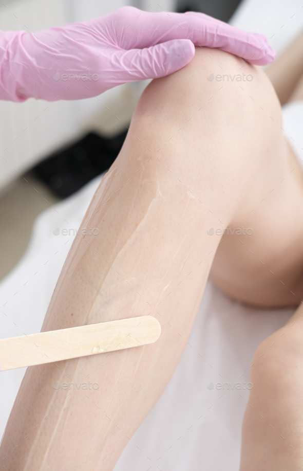 hands wearing protective medical gloves applying gel using spatula on woman's leg - Stock Photo - Images