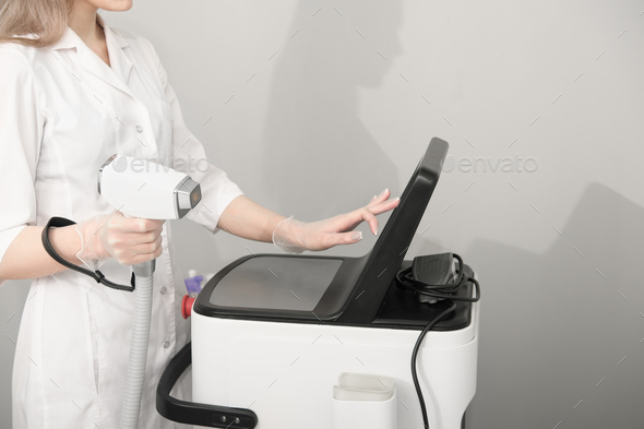 woman wearing white medical uniform holding laser epilation machine device.