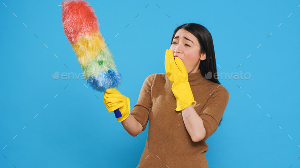 Tired professional maid cleaning furniture dust using colorful duster during cleaning session