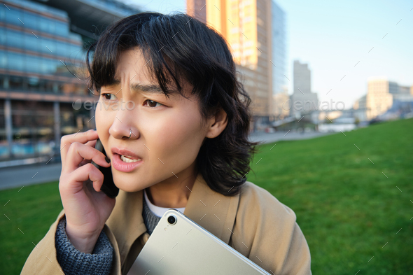 Close up portrait of young asian woman talks on mobile phone with concerned face, hear bad news
