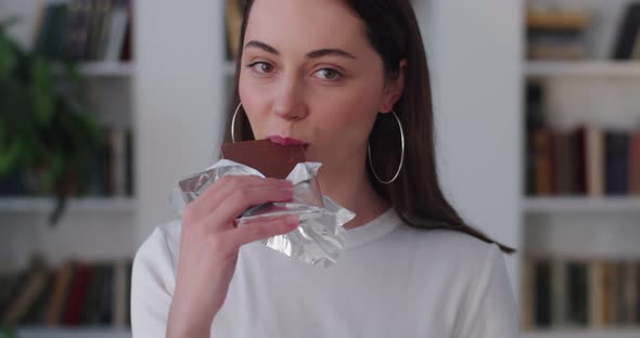 Young Caucasian Woman Eating Chocolate Bar Close Up Indoors Apartment Background