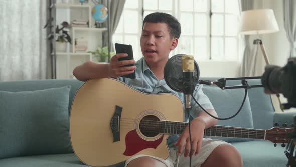 Asian Boy Is A Vlogger With Guitar Read Comment On Mobile Phone. The Boy Is Streaming alt