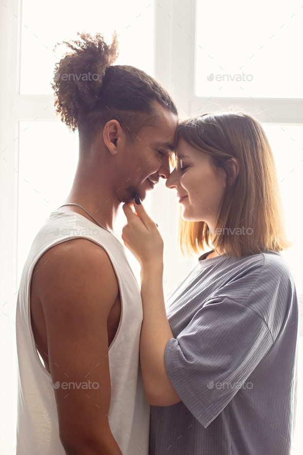 Portrait of a multiracial couple, boyfriend and girlfriend face to face, stand near the window