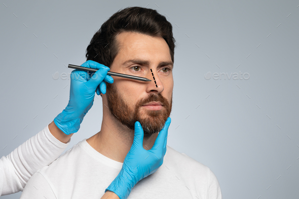 Doctor in protective gloves drawing marks on man's nose for cosmetic surgery operation, grey