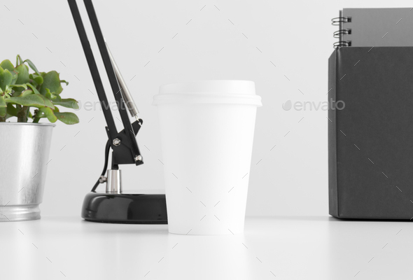 Coffee paper cup mockup with workspace accessories and a succulent in a pot on the white table.