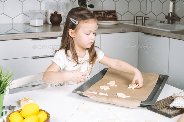 Portrait of little studiously kid girl, sitting chair kitchen, making different easter shape dough