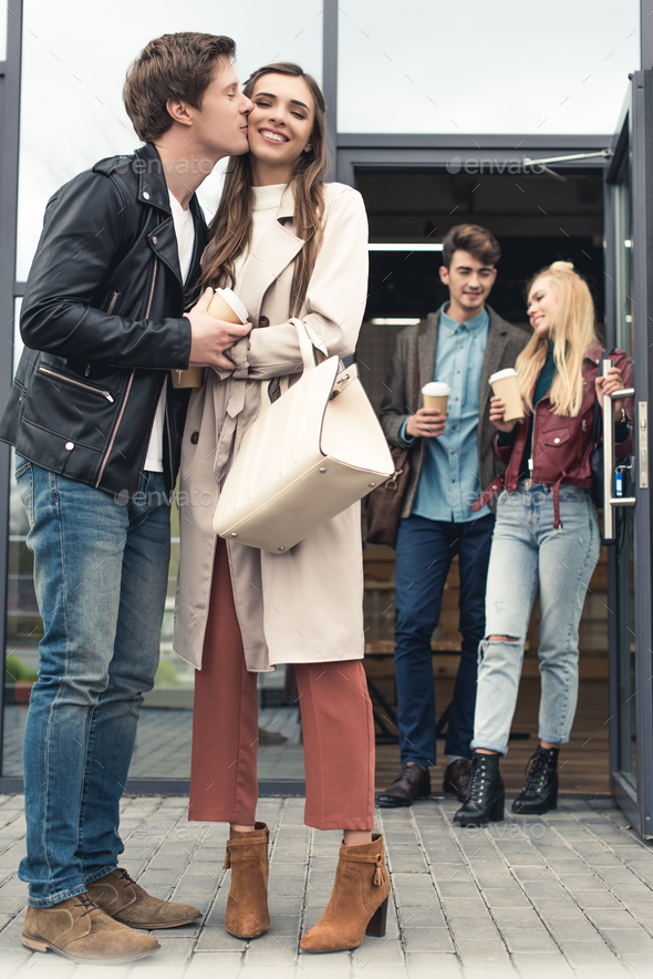 Boyfriend kissing girlfriend on a street, another couple going out from