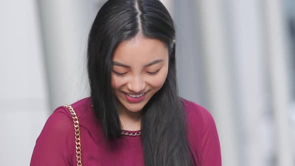 Asian woman looking down at her phone and laughing and smiling in slow motion alt