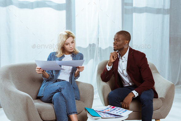 interracial photographers choosing photos together while sitting in  armchairs in office Stock Photo by LightFieldStudios