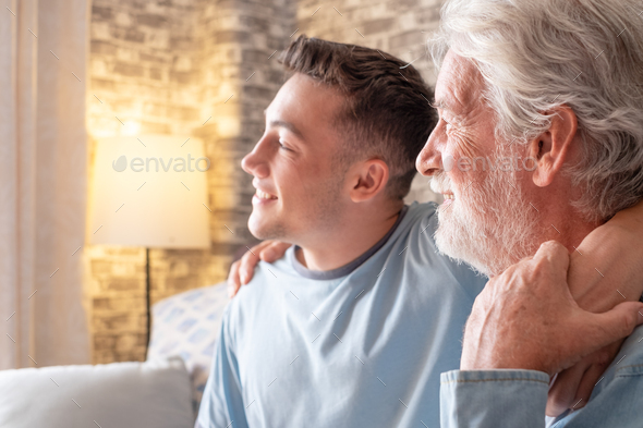 Young boy and his white-haired grandfather smile while sitting on the sofa at home