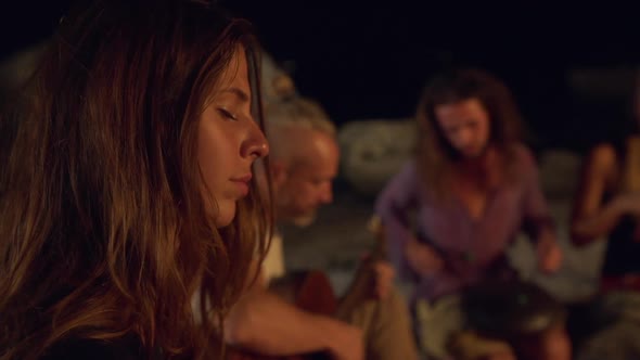 Friends Speaking Smiling Playing on Instruments Sitting Near Bonfire at Night Beach alt