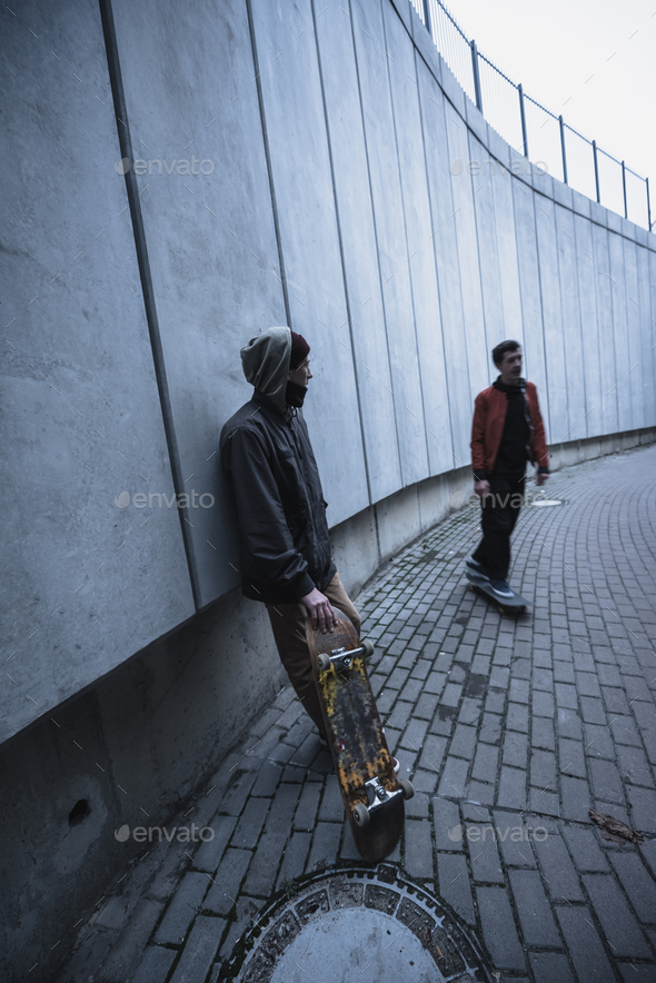 young professional skateboarders in street outfit spending time in urban landscape