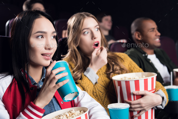 young emotional friends with popcorn watching film in movie theater
