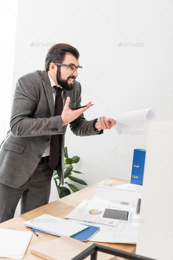 irritated businessman holding documents and screaming at someone
