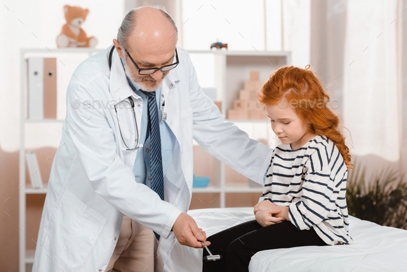 senior pediatrician in white coat examining little patient with reflex hammer in clinic