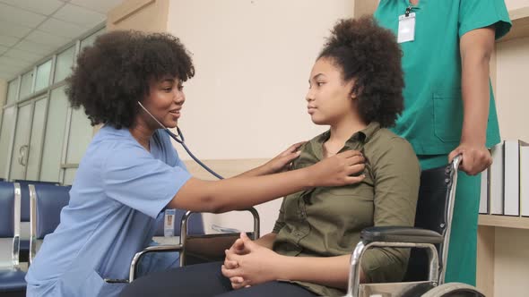 African American female doctor checks patient girl in wheelchair at hospital. alt