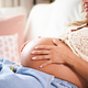 Sweet photo focus on the belly of pregnant lady cuddling her belly while  lying on the sofa at home. Stock Photo by Gigidelgado