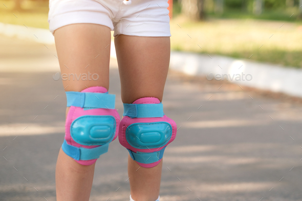Close-up of pink and blue protective knee pads on girl\'s legs.