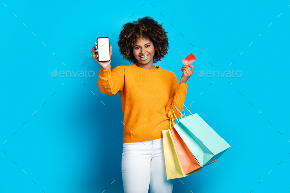 Excited lady with shopping bags showing phone and credit card