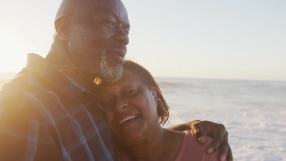 Smiling senior african american couple holding hands and dancing on sunny beach alt