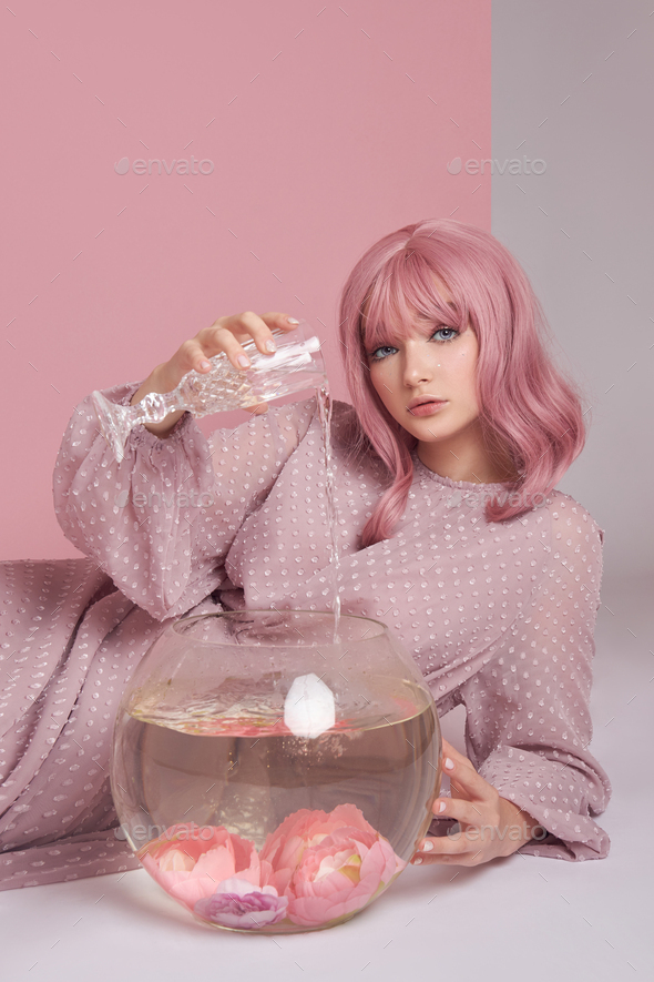 Girl with dyed pink hair in long dress sitting on the floor with a round aquarium. Portrait woman