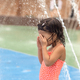 Little toddler girl standing under fountains at the playground - PhotoDune Item for Sale