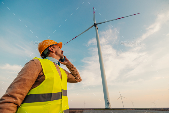 Man in uniform talking on mobile on farm with wind turbines - Stock Photo - Images