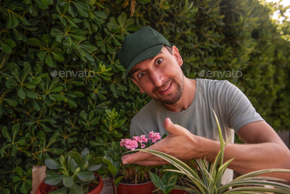 Man gardener in green cap smiles as smells indoor plants. Allergy to flowers. Natural holiday gift.