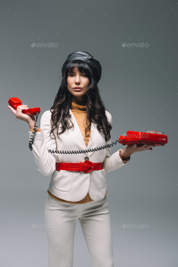 attractive brunette woman in white suit with red landline phone isolated on gray