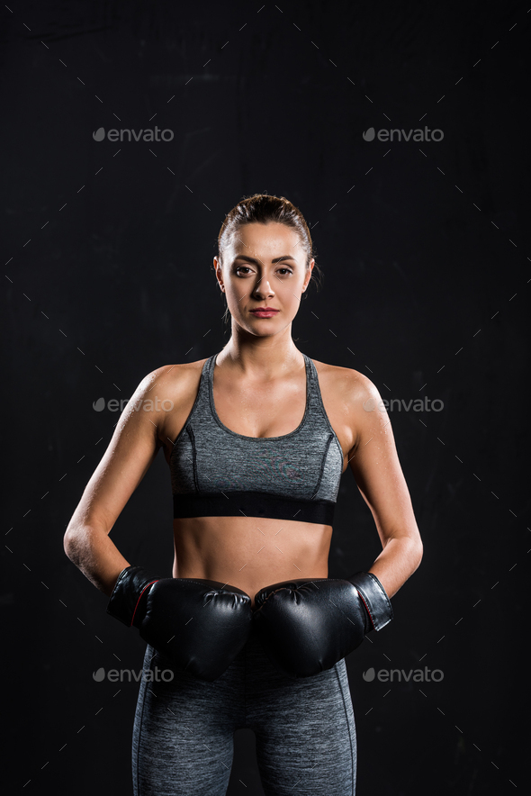 athletic sportswoman in boxing gloves looking at camera isolated on black