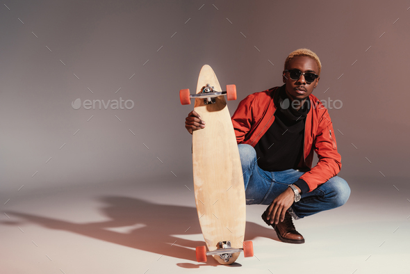 svinge indsats Anvendelse Stylish young african american skateboarder sitting and holding longboard  Stock Photo by LightFieldStudios