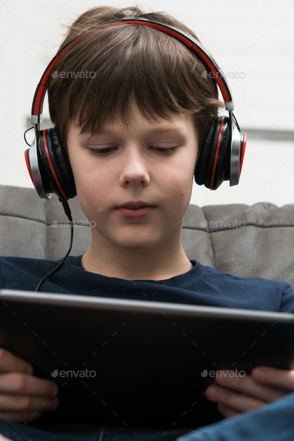 Smiling brunette little boy in wired headphones watch movies