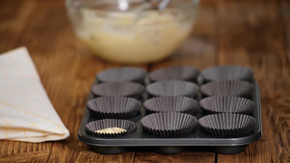 Hands pouring dough into molds for muffins on a wooden table alt