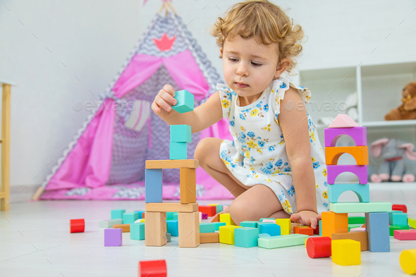 The child plays in the children\'s room with a wooden constructor. Selective focus.