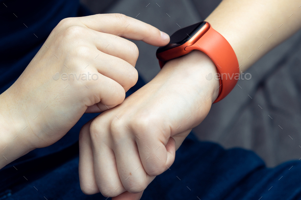 Unrecognizable teenager male hand typing on red smart watch on hand, wrist watch technology. Call