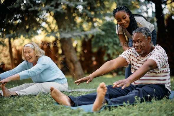 Happy black physical therapist assisting seniors during exercise class in  the park. Stock Photo by drazenphoto