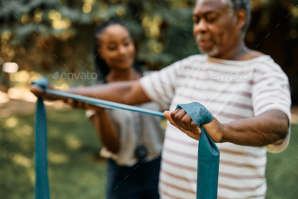 Close up of black senior using resistance band during physical therapy at nursing home\'s park.