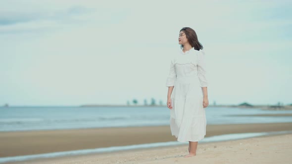 Cute Asian girl walking on the beach by the beach. She turned to smile at the camera.