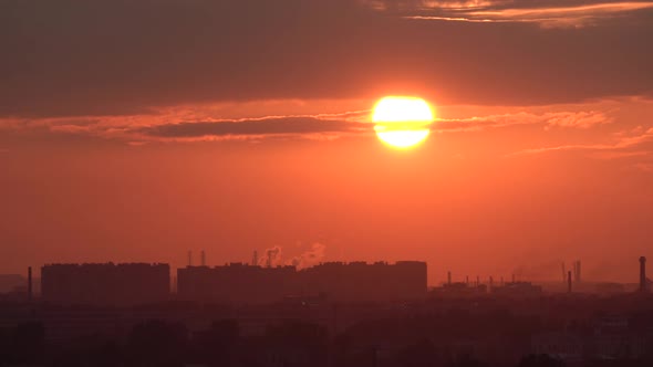 Sun Comes Down From Behind a Cloud and Sets Over the Horizon Against the Backdrop of an Industrial