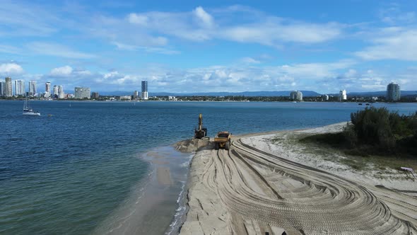 Moving drone view of heavy machinery working on a coastal rejuvenation project with a city skyline i alt
