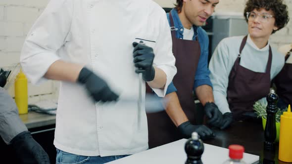 Male Chef Sharpening Knife in Kitchen During Master-class in Cookery School alt