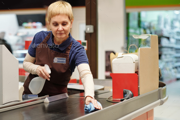 Mature female cashier spraying sanitizer on checkout line