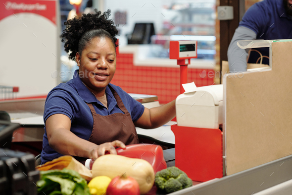 Young African American shop assistant taking food products from checkout line