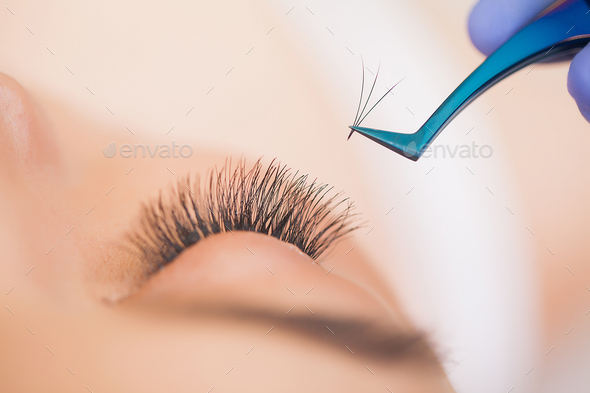 Professional stylist lengthening female lashes. Master and a client in a beauty salon.